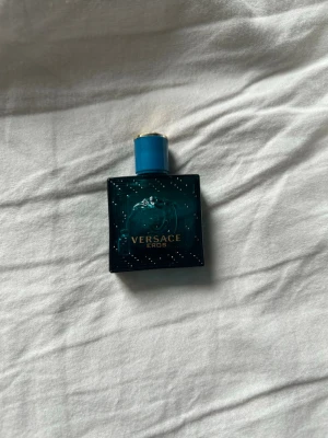 Versace Eros parfym 5ml - Versace Eros parfym i en liten, fyrkantig flaska på 5ml. Flaskan är turkosblå med gulddetaljer och har ett elegant Medusa-huvud på framsidan. Lock i matchande blått med guldfärgad topp. Perfekt storlek för att ta med sig.