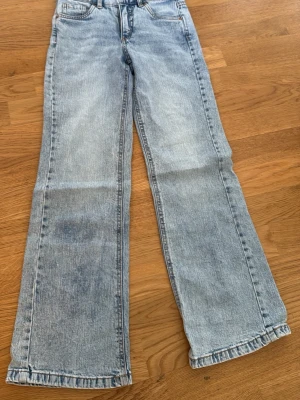 Ljusblå utsvängda jeans - Säljer ett par ljusblå jeans med utsvängda ben och klassisk femficksmodell. Jeansen har knappfickor i bak och raka sömmar, perfekta för en avslappnad och trendig look. Materialet är klassisk denim i bomull.