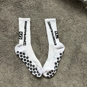 Vita FS Footballsocks med grepp - Säljer ett par vita FS Footballsocks med svart text längs sidan och grepp på undersidan. Perfekta för dig som vill ha extra fäste i skorna, oavsett om du lirar fotboll eller bara vill ha sköna strumpor. Klassisk modell i sportig stil.