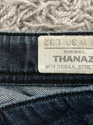 Mörkblå Diesel Thanaz jeans - Säljer ett par mörkblå smala jeans från Diesel, modell Thanaz. Jeansen har klassisk femficksdesign, diskreta slitningar och tvättade detaljer för en cool look. Materialet är denim med stretch för extra komfort.