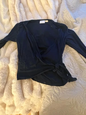 Mörkblå omlottopp från Gina Tricot - Snygg mörkblå knytkofta från Gina Tricot med lång ärm och knyt i sidan. Perfekt för dig som gillar en enkel men trendig look. Tunn och mjuk i materialet, passar till många olika outfits.