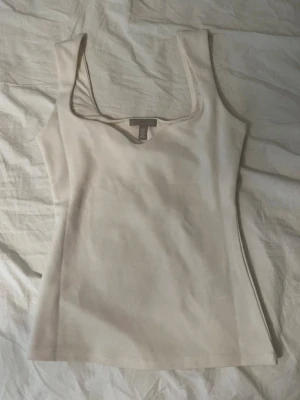 Beige ribbad linnetopp  - Snygg beige linnetopp med ribbad struktur och djup rundad halsringning. Toppen är ärmlös och har en figurnära passform.