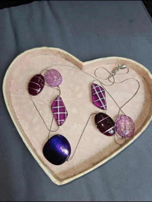 lila halsband - Unikt halsband med stora lila och mörklila glaspärlor/stenar i olika former. Några pärlor har ett rutigt mönster i silver och andra är transparenta med spräcklig effekt. Kedjan är tunn och silverfärgad. Perfekt accessoar för dig som vill sticka ut.  Kan även hämtas I Partille  J