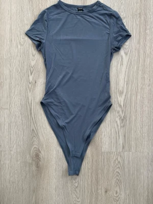 Mörkgrå basic kortärmad body - En enkel och stilren mörkblå body med korta ärmar och rund hals. Tillverkad i mjukt material som sitter tight mot kroppen. Perfekt att styla med jeans eller kjol för en clean look.