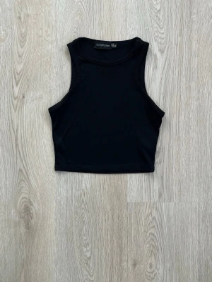 Svart ribbad croppad linnetopp - Snygg svart croppad linnetopp med ribbad struktur och ärmlös design. Perfekt att matcha med höga jeans eller kjol för en clean och trendig look.