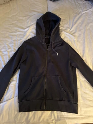 Mörkblå hoodie från Polo Ralph Lauren - Snygg mörkblå hoodie från Polo Ralph Lauren med dragkedja, kängurufickor och klassisk vit logga broderad på bröstet. Tillverkad i mjuk bomullsblandning. Finns inga defekter och köptes ny för ungefär 2000. 