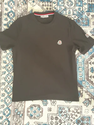 Svart Moncler t-shirt med logga - Svart t-shirt från Moncler med klassisk rund hals och liten broderad Moncler-logga på bröstet samt ärmen. Enkel och stilren design som passar till det mesta. T-shirten har korta ärmar och är tillverkad i mjukt material.