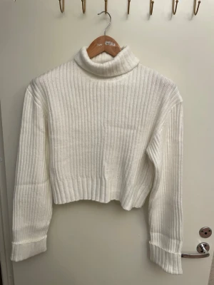 Vit ribbstickad polotröja FB Sister, stl M, helt ny  - Vit ribbstickad polotröja från FB Sister med croppad passform och långa ärmar. Tröjan har en hög polokrage och är tillverkad i ett mjukt, stretchigt material som känns skönt mot huden. Perfekt för lager-på-lager och en clean look. Stl M