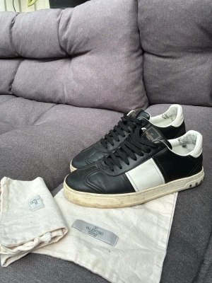 Svarta och vita sneakers från Valentino - Snygga svarta sneakers från Valentino med vit sidopanel och vita detaljer. Skorna har svarta skosnören, vit insida och en beige sula. Tillverkade i läder och levereras med original dustbags från Valentino. Alla nitar sitter kvar.