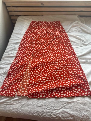 Röd långkjol med vita prickar - Snygg röd långkjol med vita prickar och en slits framtill. Kjolen har en utsvängd passform och är perfekt för dig som vill sticka ut med ett färgglatt mönster. Tillverkad i ett lätt och skönt material som passar bra till varmare dagar. Köpt på SHEIN och använd endast en gång. Nypris är 129, mitt pris är 29, köparen står för frakt. 