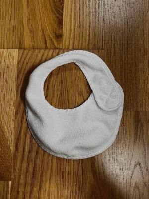 Vit dregglis från H&M - Praktisk vit dregglis från H&M med stilren och enkel design. Perfekt för att hålla kläderna torra från dreggel och måltider! Försluts smidigt med kardborreband! Material: Yttertyg: 80 % Bomull och 20 % Polyester. Foder: 100 % Polyester. Storlek: One Size. Säljs i bra skick! Kika gärna in på mina andra annonser, jag säljer just nu flera barn- och babyprodukter! Hör av dig vid frågor och intresse!