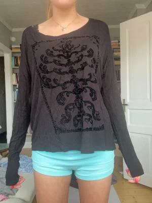 Svart långärmad tröja med sammetstryck - Svart långärmad tröja med unikt sammetstryck i barockstil på framsidan. Tröjan har en lös passform, bred halsringning och långa ärmar. Perfekt för dig som gillar en lite alternativ och avslappnad stil.
