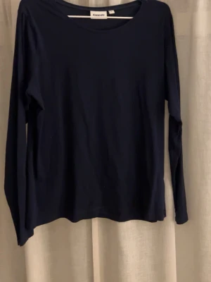 Mörkblå långärmad topp Kappahl - En enkel och stilren mörkblå långärmad topp från Kappahl. Toppen har rund halsringning och är tillverkad i mjukt bomullsmaterial. Perfekt basplagg att matcha med olika outfits.