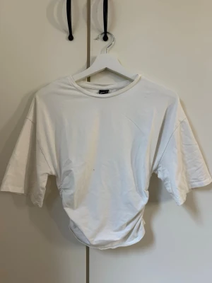 Vit t-shirt med resår på sidorna. - Enkel och clean vit t-shirt med oversized passform, resår på sidorna och korta ärmar. Tillverkad i mjuk bomull, perfekt för en avslappnad och stilren look. Klassisk rund halsringning och inga synliga tryck eller detaljer. Den är endast använd 1 gång.