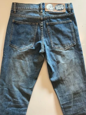 Blå jeans från Cheap Monday - Ett par klassiska blå jeans från Cheap Monday i rak modell. Jeansen har fem fickor, bälteshällor och en knappgylf. Tillverkade i slitstark denim med en snygg tvättad look och tydliga sömmar. Perfekta för en avslappnad och trendig stil.