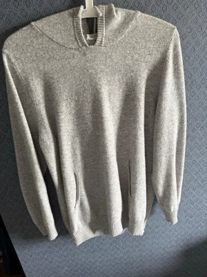 Ljusgrå Kashmir hoddie  - En stilren ljusgrå hoodie i mjukt material. Hoodien har en klassisk huva och två diskreta fickor framtill. Perfekt för en avslappnad look och enkel att matcha med andra plagg. Passar 165-175cm lång. Lagad vid främre nacke.