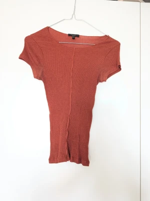 Rostfärgad top Massimo dutti - Säljer en ribbad topp i en snygg rostfärgad ton. Toppen har korta ärmar, rund halsringning och en dekorativ söm framtill. Materialet är stretchigt och bekvämt, perfekt till jeans eller kjol.