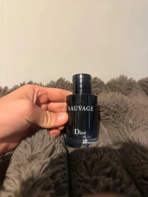 Dior Sauvage parfym  - Säljer en Dior Sauvage parfym i en elegant mörkblå glasflaska med svart lock. Flaskan har en stilren och modern design med tydlig logga framtill. Doften är populär och passar dig som gillar fräscha och maskulina toner.