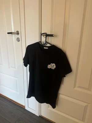 Moncler Svart t-shirt med tryck - HELT ÄKTA KÖPT PÅ NK för 2200:- STORLEK S. Passar dig om du är under 175. ANVÄND ett antal gånger. Snygg svart t-shirt med korta ärmar och ett litet tryck på bröstet. Enkel och stilren design som passar perfekt till jeans eller shorts. T-shirten har en klassisk passform och rund halsringning.