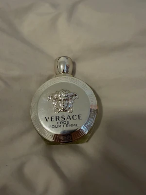 Versace Eros Pour Femme parfym - Lyxig parfym från Versace, Eros Pour Femme, i en rund flaska med silverfärgad kant och Medusa-huvud i mitten. En sensuell, passionerad och strålande doft med citroner från Sicilien och jasmin. I hjärtat finner vi mjukare toner av apelsinblomma och mangolia. Basen är sensuell med toner av vit patchouli och mysk.