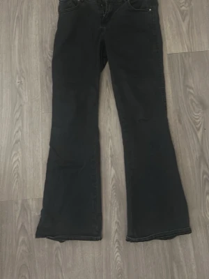 Svarta bootcut jeans - Säljer ett par svarta bootcut jeans med klassisk femficksmodell och normal midja. Jeansen har utsvängda ben och är tillverkade i ett mjukt denimtyg som ger en skön passform. Köpte från lager. En av fickorna knappar är sönder, så går ej att knäppa.