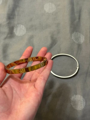 Guldigt armband med skruvdetaljer - Snyggt armband i guldfärgad metall med ingraverade skruvliknande detaljer runt om. Stilren och modern design som passar perfekt till din vardagsstil eller när du vill addera lite edge till outfiten. Armbandet är stelt och har en exklusiv känsla. Vattenfast 