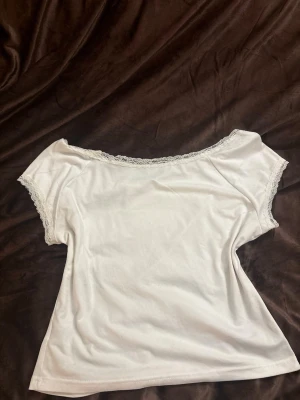 Vit offshoulder topp med spetskant - Söt vit offshoulder topp med spetsdetaljer längs halsringningen och ärmsluten. Toppen har korta ärmar. 