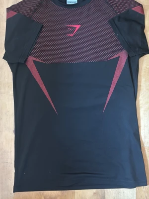 Gymshark Onyx Compression Shirt  - Snygg svart och röd Gymshark Onyx compression shirt. Perfekt för träning och gym då den sitter tajt och följer kroppen. Använd men i mycket fint skick. Storlek S.