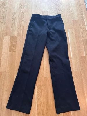 Svarta los waist kostymbyxor med pressveck - Snygga svarta low waist kostymbyxor med klassiskt pressveck och raka ben.  Perfekta för en stilren look och passar till skjorta eller t-shirt. Materialet ser ut att vara en blandning av polyester och bomull.