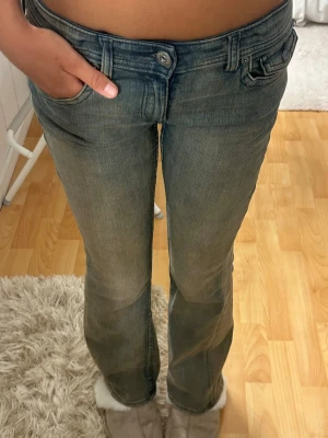 Bootcut jeans med låg midja - Snygga blå bootcut jeans med låg midja och klassiska fem fickor. Jeansen har en liten ficka med lock och knappdetalj framtill. Tillverkade i denim med lätt tvättad look och raka ben. Perfekta för en avslappnad och trendig stil.