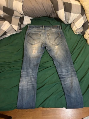 Blå slitna jeans med raka ben - Säljer ett par blå dondup George jeans med snyggt slitna detaljer. Jeansen har två bakfickor med dragkedja och klassisk denim-look. Perfekta för dig som gillar en avslappnad och trendig stil.