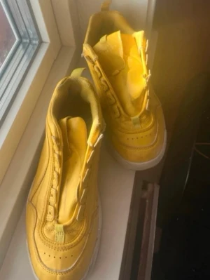 Gula chunky sneakers med platåsula - Säljer ett par gula sneakers med tjock vit platåsula och detaljerade sömmar. Skorna har en låg modell och är tillverkade i syntetmaterial med mesh och läderlook. Perfekta för dig som vill sticka ut med färg och chunky stil.