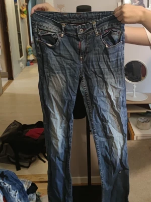 Snygga Bondelid jeans i strl 30 – Y2K vibe!  - storlek 30. De har en jättesnygg blå tvätt med ljusare slitningar över låren och klassiska detaljer, bland annat den lila broderade texten på insidan av linningen.