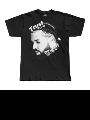 Svart t-shirt med tryck och text - Cool svart t-shirt med stort grafiskt tryck framtill som föreställer ett porträtt och texten 'Trust'. T-shirten har klassisk passform, rund hals och korta ärmar. Perfekt för dig som gillar streetwear och vill sticka ut.