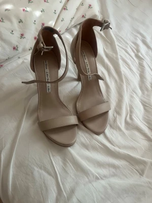 Beige pumps med ankelrem och klack - Säljer ett par stilrena beige högklackade klacksor med öppen tå, smal rem över tårna och justerbar ankelrem med silverfärgat spänne. Stl 36, kommer aldrig till användning och endast testade. Köpta för 750kr därför priset, men det går att diskutera.