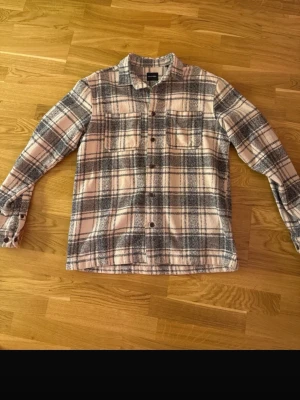 Rutig skjorta i beige och grå - Säljer en snygg rutig skjorta i beige och grå toner. Skjortan har långa ärmar, klassisk krage, knappar framtill och en bröstficka. Perfekt för dig som gillar en avslappnad men stilren look.