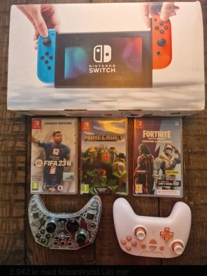 Nintendo Switch med spel och kontroller - Nintendo Switch med blå och röd Joy-Con, originalkartong, tre spel (FIFA 23, Minecraft, Fortnite) samt två extra handkontroller – en transparent och en vit med orange knappar. Perfekt för gaming och multiplayer.