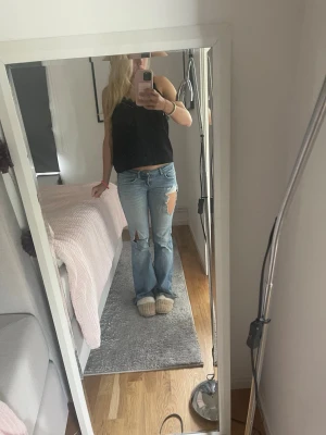 Ljusblå slitna bootcut jeans - Säljer ett par ljusblå bootcut jeans med stora slitningar på låret och knät. Jeansen har låg midja och klassisk femficksmodell. Perfekta för en avslappnad och trendig look. Materialet är denim i bomull.