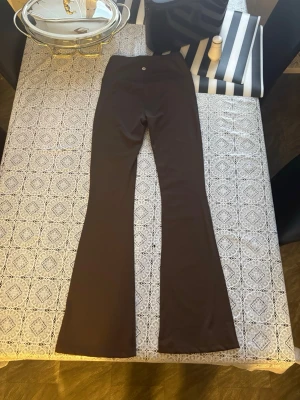 Bruna flared leggings från Lululemon - Snygga bruna leggings från Lululemon i modellen Groove Super-High-Rise Flared Pant. De har hög midja och utsvängda ben, tillverkade i det mjuka och stretchiga Nulu-materialet som känns superbekvämt. Perfekta för en trendig och avslappnad look.