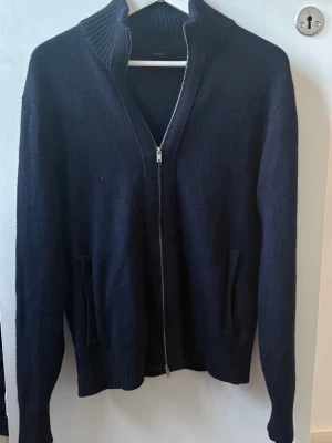 Massimo Dutti tröja - Mörkblå stickad ziptröja från Massimo Dutti med hög ribbad krage och två fickor framtill. Tröjan har långa ärmar och ribbade muddar vid ärmslut och nederkant. Perfekt för lager på lager och enkel att matcha.