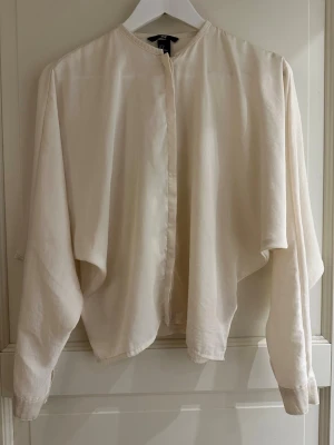 Krämvit blus från H&M, storlek 36 - Säljer en elegant, krämvit blus från H&M i storlek 36. Blusen har långa ärmar, rund halsringning och knäppning framtill. Passar perfekt till både vardag och fest! Skick: mycket bra, sparsamt använd. Breda armar ”vingar” 