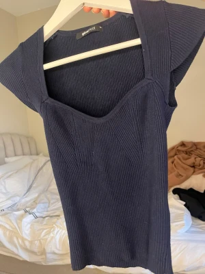 Mörkblå ribbad topp Gina Tricot - Snygg mörkblå ribbad topp från Gina Tricot med v-ringad hals och korta ärmar. Toppen har en croppad passform och är tillverkad i stretchigt material som sitter bekvämt. Perfekt att styla med jeans eller kjol för en trendig look.