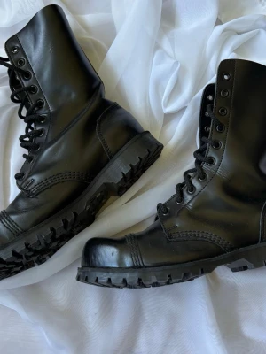 Underground England Boots / Kängor 10-eye Steel Cap UK7 - Rätt skor för kommande punk-festivaler! Underground England Original Steel Toe, modell UR-7703-BLK, svarta 10-håls kängor med grov commando-sula. Köpta från England för många år sedan, sparsamt använda. Sulan nästan oanvänd, se bilder. Storlek UK 7. Äkta läder, made in England. Ligger i kategorin skor/dam men är ju mer unisex. Nypris ca £180.