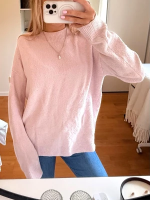 Ljusrosa oversized stickad tröja - Mysig ljusrosa stickad tröja med oversized passform och långa ärmar. Tröjan har rund halsringning och ribbade muddar vid ärmslut och nederkant. Perfekt för lager på lager och en avslappnad look. Den är nopprig därav det låga priset