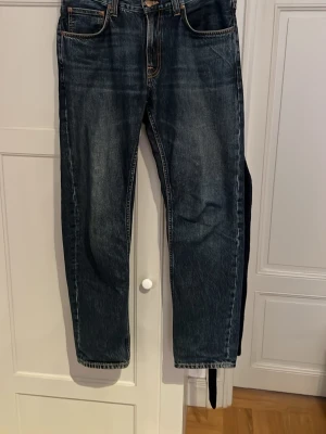 Nudie jeans  - Säljer ett par mörkblå jeans med raka ben och klassisk femficksmodell. Jeansen har kontrastsömmar och en lätt tvättad look. Perfekta för en avslappnad och stilren outfit. Modell Gritty Jackson 100% bomull. Storlek W32 L32