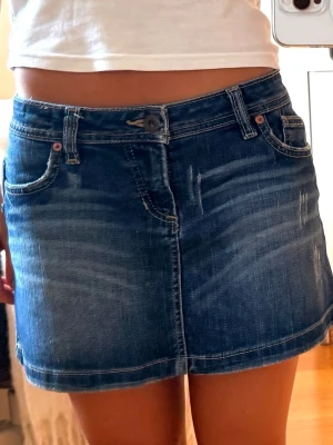 Blå jeanskjol från Volcom - Snygg blå jeanskjol från Volcom med klassisk femficksdesign och slitna detaljer framtill. Kjolen har bälteshällor och stängs med knapp och dragkedja. Perfekt för dig som gillar en avslappnad och trendig stil.