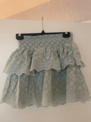 Ljusgrön volangkjol med broderi - Supersöt ljusgrön kortkjol med volanger och broderade detaljer. Kjolen har elastisk midja och ett romantiskt hålmönster som ger en somrig vibe. Perfekt för dig som gillar feminina och trendiga plagg.