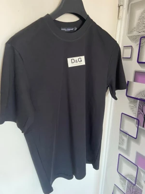 Svart D&G t-shirt med logga - Snygg svart t-shirt från Dolce & Gabbana med klassisk D&G-logga på bröstet. T-shirten har rund hals och korta ärmar, perfekt för en clean och stilren look. Tillverkad i mjuk bomull som känns skön mot huden.