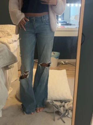Blå bootcut jeans - Säljer ett par ljusblå bootcut jeans med stora slitningar över knäna och lätt slitna detaljer. 