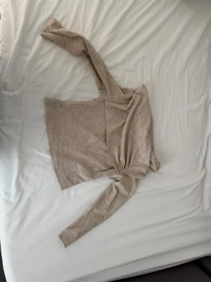 Beige oneshoulder topp från SHEIN - Trendig beige oneshoulder topp från SHEIN med lång ärm och croppad passform. Tillverkad i mjukt syntetmaterial som känns skönt mot huden. Perfekt för dig som vill ha en stilren och modern look.
